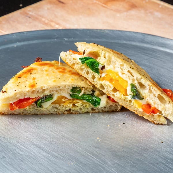 Two halves of a calzone filled with melted cheese, spinach, and red and yellow peppers.