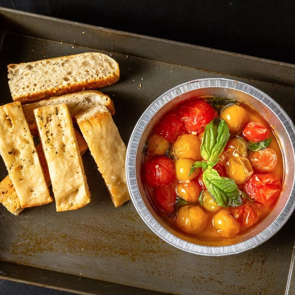 Baked red and yellow cherry tomatoes with basil in a foil tin, served with focaccia bread.