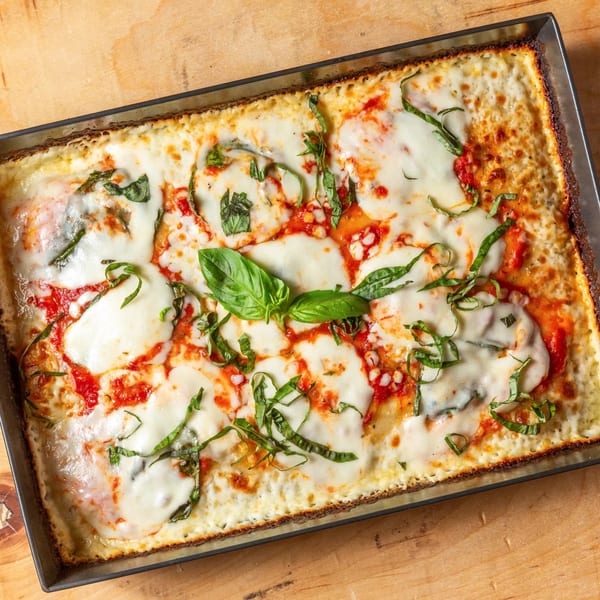 A rectangular Main Street Pizza with melted mozzarella, red sauce, and fresh basil in a metal pan.