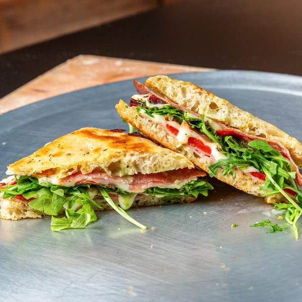 Two halves of a sandwich with meat, cheese, red peppers, and arugula on focaccia bread.