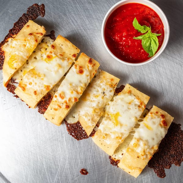 Cheesy breadsticks with crispy edges and a side of red marinara sauce with basil.