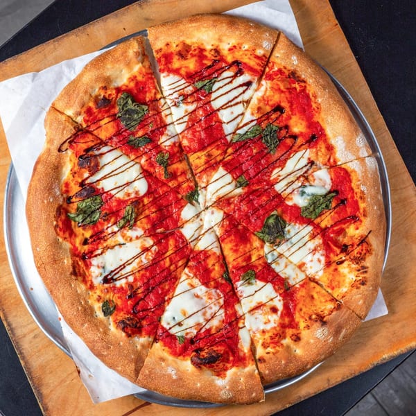 Main Street Pizza's sliced Margherita pizza with fresh basil, mozzarella, and balsamic glaze on a wooden board.
