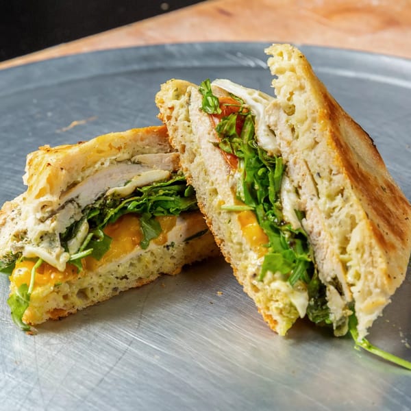 A sliced chicken panini with arugula, tomatoes, and cheese on a metal surface.