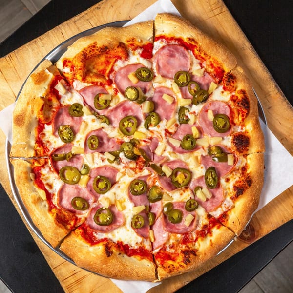 Main Street Pizza's Hawaiian pizza with ham, pineapple, and jalapeños on a wooden board.
